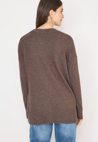 Hnědý pletený volný svetr s žebrovaným lemem a manžetami, s uvolněným střihem a spadenými rameny. Materiál má měkkou texturu.