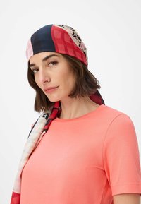 Colorful silk scarf featuring geometric patterns in blue, red, and pink draped around a light coral shirt. Smooth texture and soft drape.
