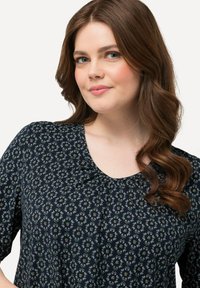Blusa floral de color marino con cuello redondo, que presenta pequeñas flores blancas y rosas en un patrón repetido, y fabricada en una tela suave y ligera.