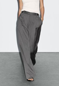 Gray pinstriped wide-leg trousers featuring front pleats and side pockets, made of a lightweight fabric, paired with a fitted white top.