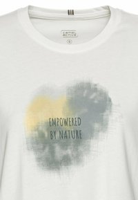 Hvid bomulds t-shirt med et tekstureret grafik i grå og gul, med teksten "EMPOWERED BY NATURE" i sort centralt placeret.