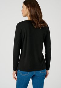 Zwarte lange mouwen shirt, zachte katoenstof, ronde halslijn, getailleerde snit, gedragen met blauwe jeans. Achteraanzicht toont eenvoudig ontwerp zonder versieringen.