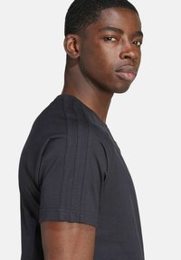 Čierne tričko s krátkym rukávom a okrúhlym výstrihom, so tromi vertikálnymi pruhmi pozdĺž ramien a jemnou, hladkou textúrou.