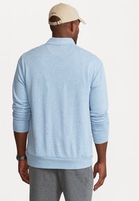 Ljusblå sweatshirt med ribbad mudd och nederkant. Mjuk, texturerad tyg. Baseballkeps med "POLO" logotyp bak.