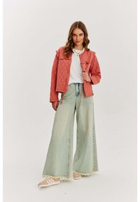 Różowa kurtka pikowana z falbankami, biała koszulka, szerokie jasnoniebieskie dżinsy z postrzępionymi końcami oraz beżowe sneakersy z białymi paskami.