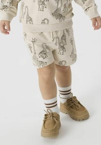Shorts beiges et sweatshirt avec un imprimé répétitif de zèbres et d'insectes. Chaussettes chevilles marron avec des rayures blanches et bordeaux et chaussures beiges.