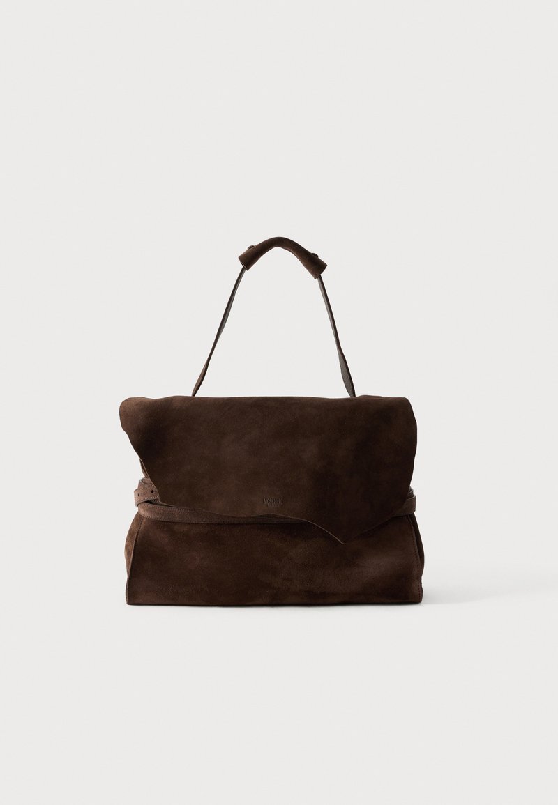 Τσάντα από σκούρο καφέ σουέντ δέρμα με ασύμμετρο καπάκι και μία χειρολαβή στην κορυφή, σε απλό φόντο.