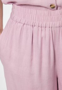 Pantalones de cintura elástica en rosa claro, hechos de una tela suave, que presentan una textura fruncida en la cintura y sutiles pliegues en el frente.