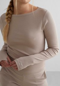 Heledadbeige pikkade varrukatega topp ribade tekstuuriga, laeva kaelusega ja liibuvate varrukatega. Omab väikest metallist aktsenti mansetil.