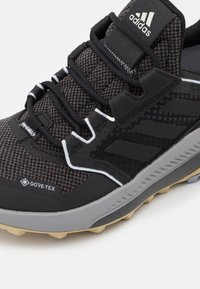 Baskets Adidas Gore-Tex noires et grises avec dessus en mesh à motifs, lacets noirs, accents blancs et semelle beige texturée.