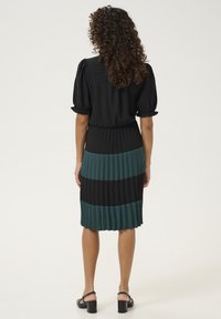 Čierne a teal plisované šaty s čiernym vrchným dielom s balónovými rukávmi a sukňou strednej dĺžky s alternujúcimi horizontálnymi pruhmi.