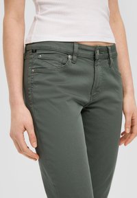 Vaqueros verdes de mezcla de algodón con un diseño ajustado, que cuentan con cinco bolsillos, una cremallera frontal y detalles sutiles de costura.