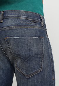 Närbild av bakfickan och midjan på blå Diesel-jeans som bärs med en grön skjorta.