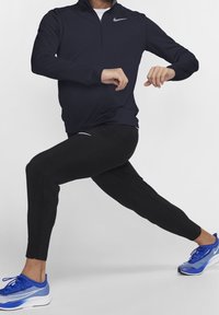 T-shirt a zip a manica lunga color navy e pantaloni neri a gamba affusolata, indossati con scarpe da ginnastica blu e bianche. Presenta una texture a coste e loghi sottili.