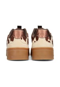 Las zapatillas marrón y crema presentan un diseño de estampado de vaca, un talón metálico en bronce y una suela de goma texturizada con ranuras horizontales.
