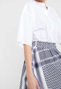 Camisa blanca de botones con mangas cortas combinada con una falda de estampado azul y blanca que presenta diseños geométricos y una cintura ajustada.