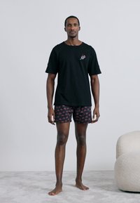 Tricou negru din bumbac cu mâneci scurte și un mic desen brodat, asortat cu pantaloni scurți cu model, având un fundal închis și accente colorate.