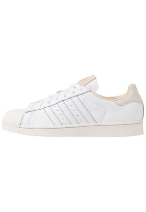 Biały niski sneaker z ochronnym noskiem, trzema przeszywanymi paskami, zapięciem na sznurowadła oraz beżowymi akcentami na pięcie i języku.