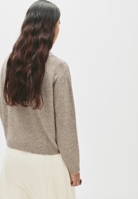 Beige villapaita pitkillä hihoilla ja ribbaamalla, puolihameen päällä, näyttää teksturoidulta neuleelta kiinteässä värissä.