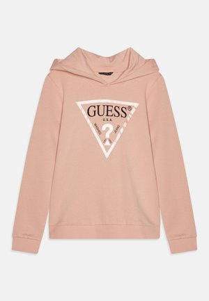 Hoodie rose clair avec un logo triangulaire blanc à l'avant portant l'inscription "GUESS U.S.A." et "Washed Jeans" entourant un point d'interrogation.