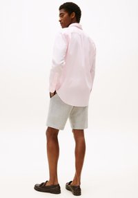 Helles rosa gemustertes Hemd mit Knöpfen, graue Shorts, dunkle Slipper; das Kleidungsstück hat lange Ärmel, Knopfmanschetten und eine lockere Passform.