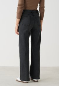 Hoge taille zwarte spijkerbroek met een relaxte pasvorm, voorzien van twee achterzakken en minimale stikdetails. Witte sneakers complementeren de outfit.