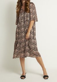 Schwarzes Midikleid mit Blumenmuster in Rosa und Weiß. Kurzärmelig, mit V-Ausschnitt und gestuftem Saum. Ein Paar schwarze Riemchensandalen.