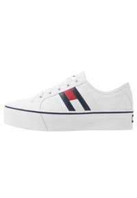 Sneakers bianche in tela con profilo basso, accenti a righe blu e rosse, punta tonda e suola in gomma testurizzata. Lacci piatti e branding minimale.