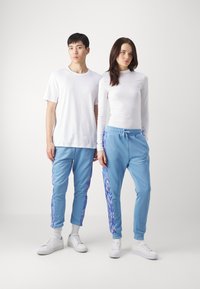 Light blue joggers with patterned side stripes, paired with white fitted tops. The joggers have an elastic waistband and tapered legs.