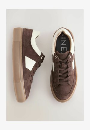 Hnedé semišové tenisky s bielymi detailmi, okrúhlou špicou, gumovou podrážkou a plochými šnúrkami. Majú textúrovaný povrch a prešívané detaily.