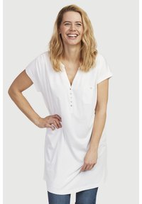 Hvid kortærmet tunika med V-hals, lomme detaljer og knaplukning. Blødt, letvægtsstof; afslappet pasform. Bæres med blå jeans.