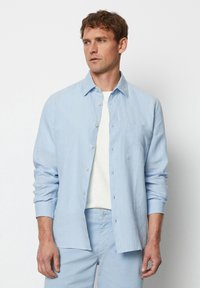  Lichtblauw linnen shirt met een knoopsluiting aan de voorkant, een klassieke kraag en een enkele borstzak. Lange mouwen met knoopmanchetten.