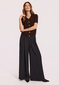Brązowy cardigan z krótkim rękawem i detalami w postaci guzików, połączony z szerokimi czarnymi spodniami. Cardigan ma luźny krój i miękką fakturę.