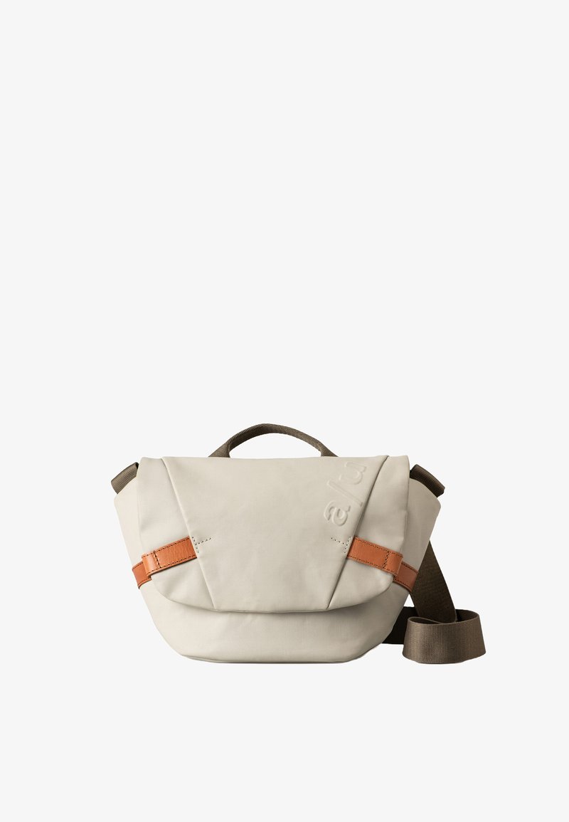 Beige Schultertasche aus robustem Stoff mit einem braunen Lederakzentriemen. Verfügt über eine strukturierte Form und einen oberen Griff zum Tragen.