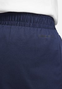 Marina atletiska byxor med elastisk midja. Har en slät yta och tryckt "Dri-FIT"-logotyp i svart nära midjan.