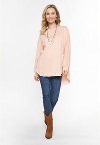 Lyserød langærmet top med et struktureret design, parret med mørkeblå skinny jeans og brune ruskinds ankelstøvler.