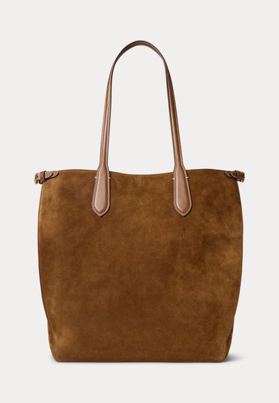 Sac fourre-tout en daim marron avec longues poignées en cuir et détails de boucles sur les côtés, présenté sur un fond blanc.