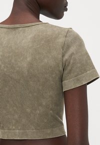 Crop top côtelé vert olive à manches courtes, avec un col rond et une texture douce. Détails de couture visibles le long du dos.