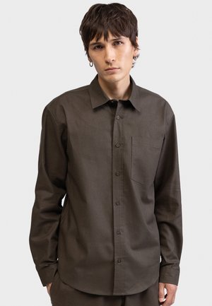 Καφέ πουκάμισο με κουμπιά, μακριά μανίκια, μια τσέπη στο στήθος και κλασικό γιακά. Λείο ύφασμα με διακριτική λάμψη.