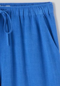 Pantalons en lin bleu avec cordon de serrage, dotés d'une taille élastique et de poches latérales, avec une finition en tissu texturé.