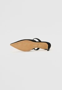 Sandalo con tacco alto in suede nero, con punta appuntita, apertura sul retro e sottile cinturino alla caviglia. Presenta una suola beige con un design testurizzato.