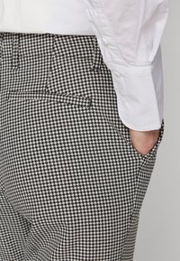 Svart och vit houndstooth-mönstrade byxor med en sidoficka. Tyget är slätt, passformen är figurnära och kombineras med en vit skjorta med knappar.