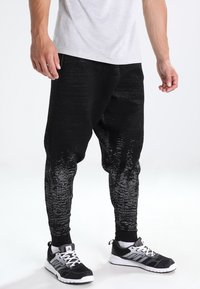 Schwarze Jogginghosen aus strukturiertem Material, mit einem Farbverlauf von reinem Schwarz bis zu hellgrau an den Knöcheln, versehen mit gerippten Bündchen.