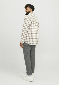 Vit och brun rutad skjorta med långa ärmar som kombineras med grå strukturerade byxor och vita sneakers, sedd från sidan och baksidan.