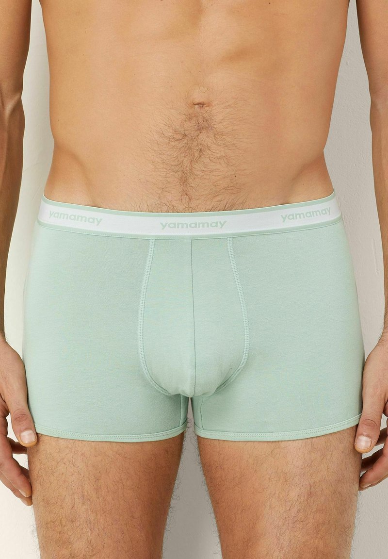 Mint vihreät boxerit, jotka on valmistettu pehmeästä kankaasta. Niissä on valkoinen vyötärönauha, jossa on "yamamay"-brändäys, ja ne ovat muodikkaat.