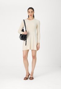 Abito a maglia a coste beige con maniche lunghe, scollo rotondo e orlo svasato. Borsa nera con tracolla e sandali con tacco marroni.