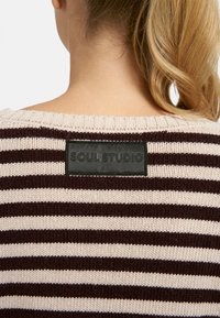 Gestreifter Strickpullover in hellbeige und dunkelbraun mit einem gerippten Ausschnitt und einem schwarzen Lederetikett mit der Aufschrift "SOUL STUDIO" auf der Rückseite.