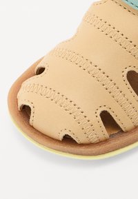 Brune lær sandal med utskårne design, sømmer og en brun såle; har en lys gul kant langs sålen.