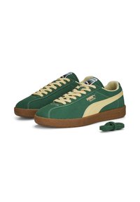 Sneakers verde in suede con strisce beige, dotate di chiusura con lacci, suola in gomma marrone testurizzata e un ulteriore laccio verde.