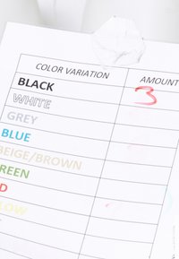 Tabella che elenca le variazioni di colore con "BLACK" e il numero 3 cerchiato con inchiostro rosso, carta bianca stropicciata sopra.